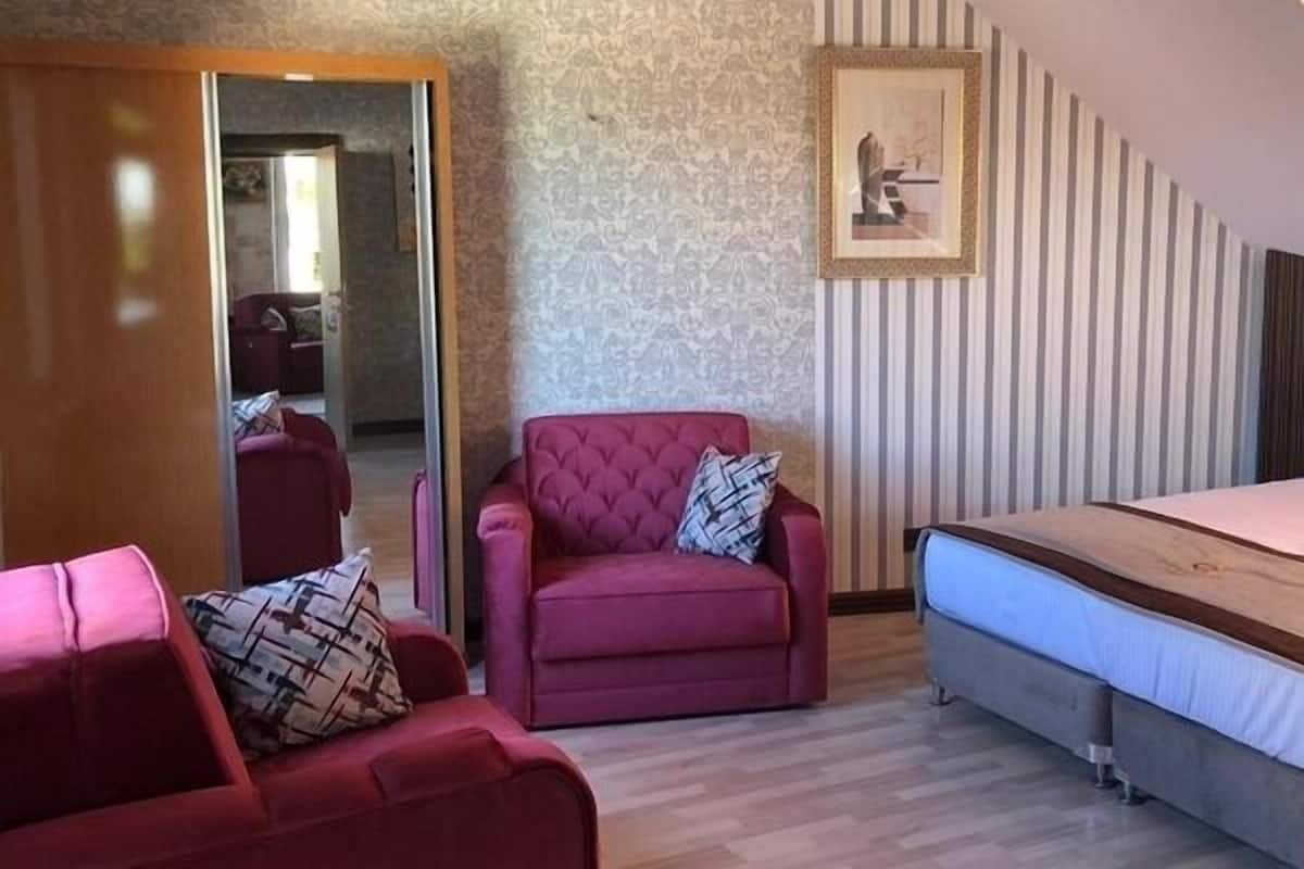 A hotel room with a bed, a red armchair, a mirror, and a ceiling light.