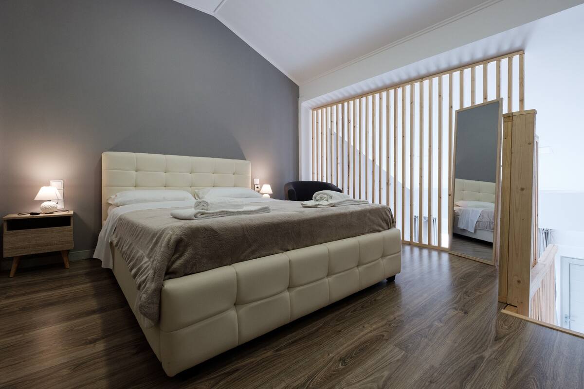Un dormitorio moderno con una cama grande, mesitas de noche y vistas a través de un separador de madera.