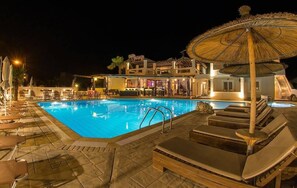Piscina amb gandules i ombrelles, envoltada d'un edifici que inclou una zona de bar.