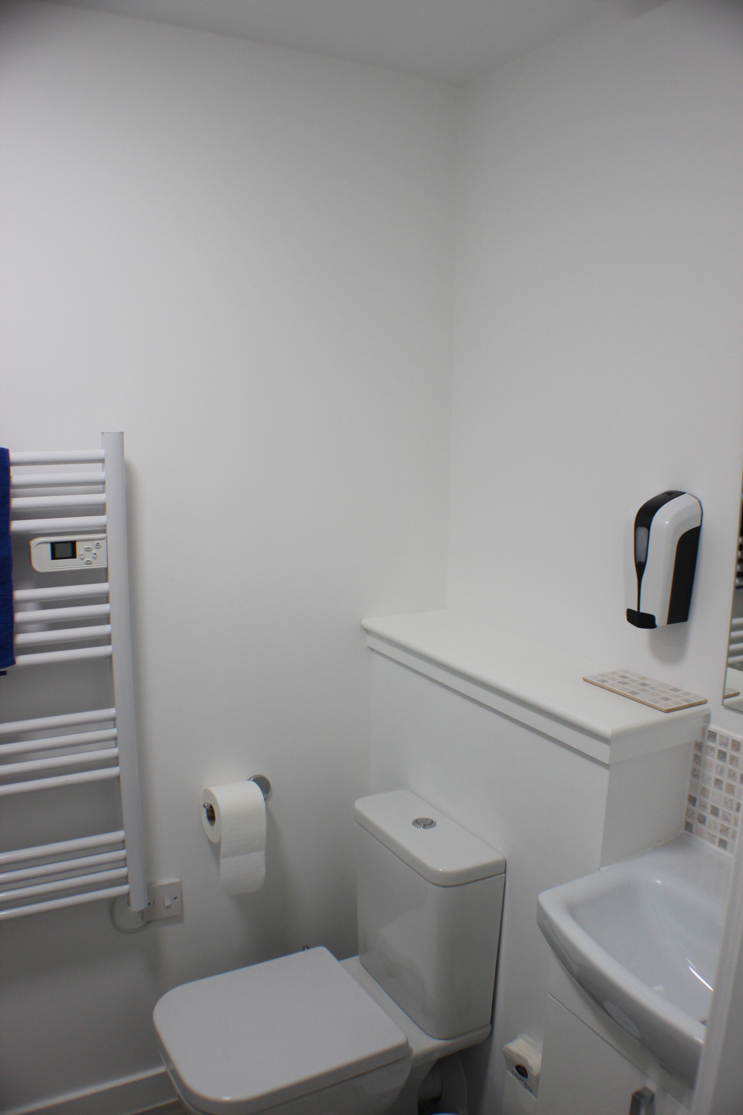 Un baño pequeño y blanco con inodoro, lavamanos y un perchero para toallas.