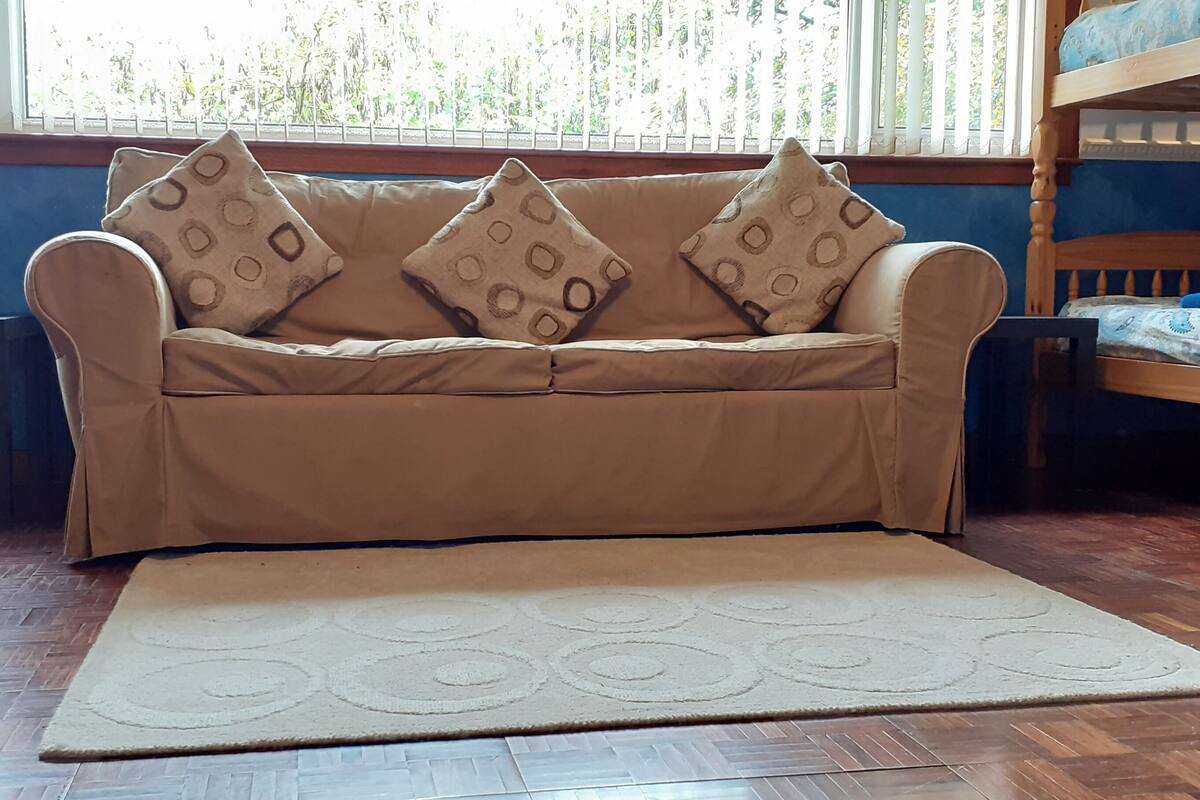 A bunk bed with a wooden headboard, a beige sofa with patterned cushions, and a wooden floor.