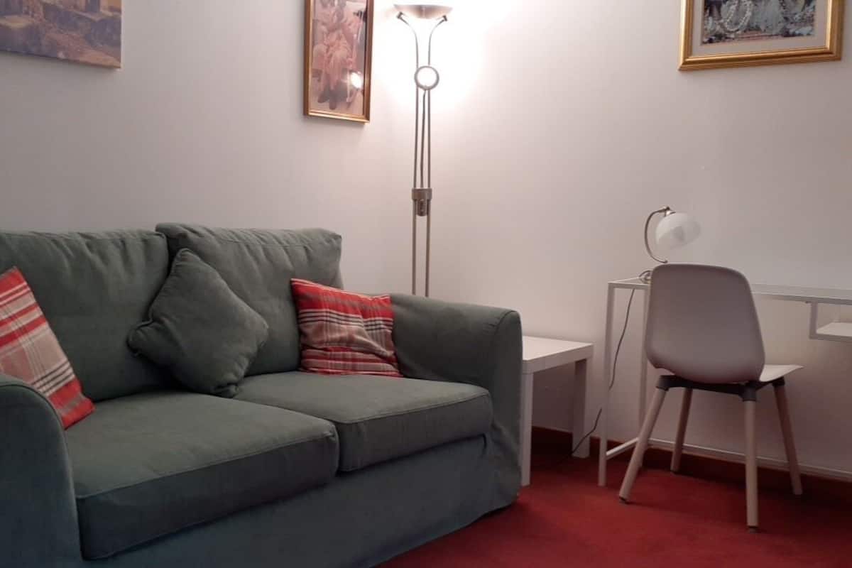 A green sofa with plaid pillows, a white desk, a grey chair, and a floor lamp.