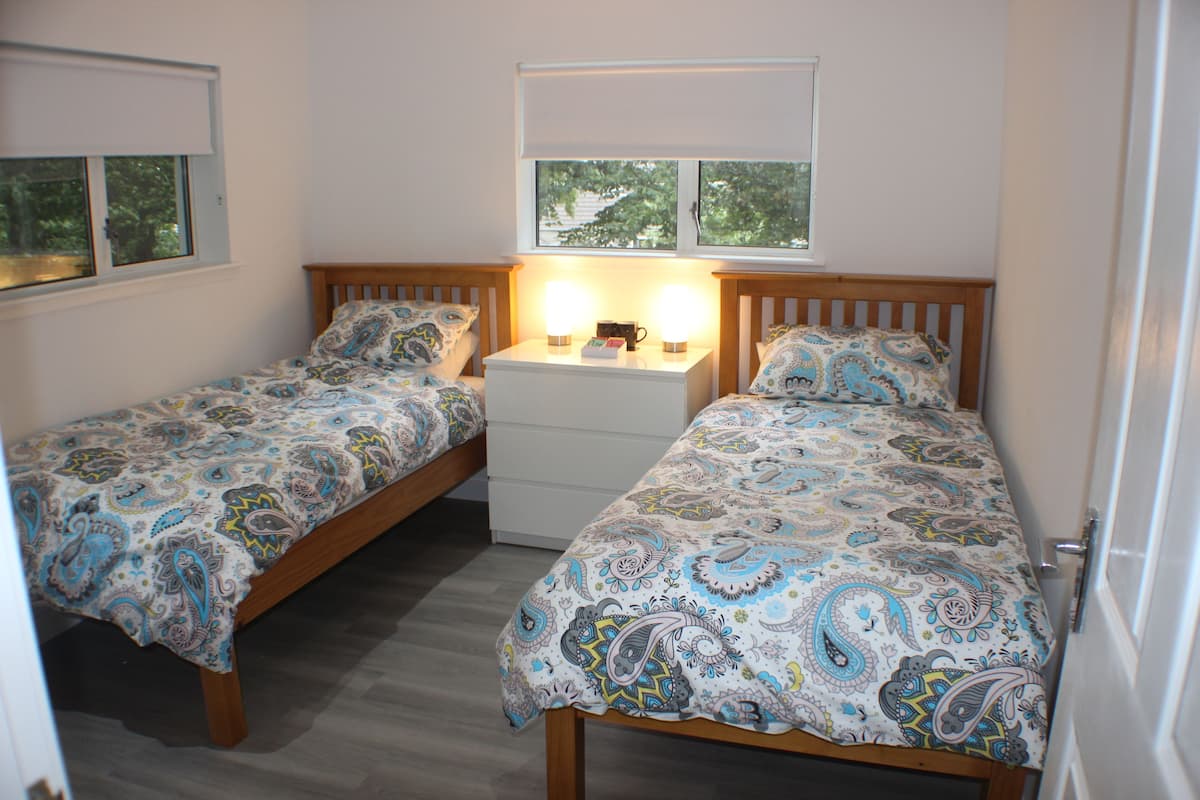A bedroom with two single beds, a nightstand, and a window with blinds.