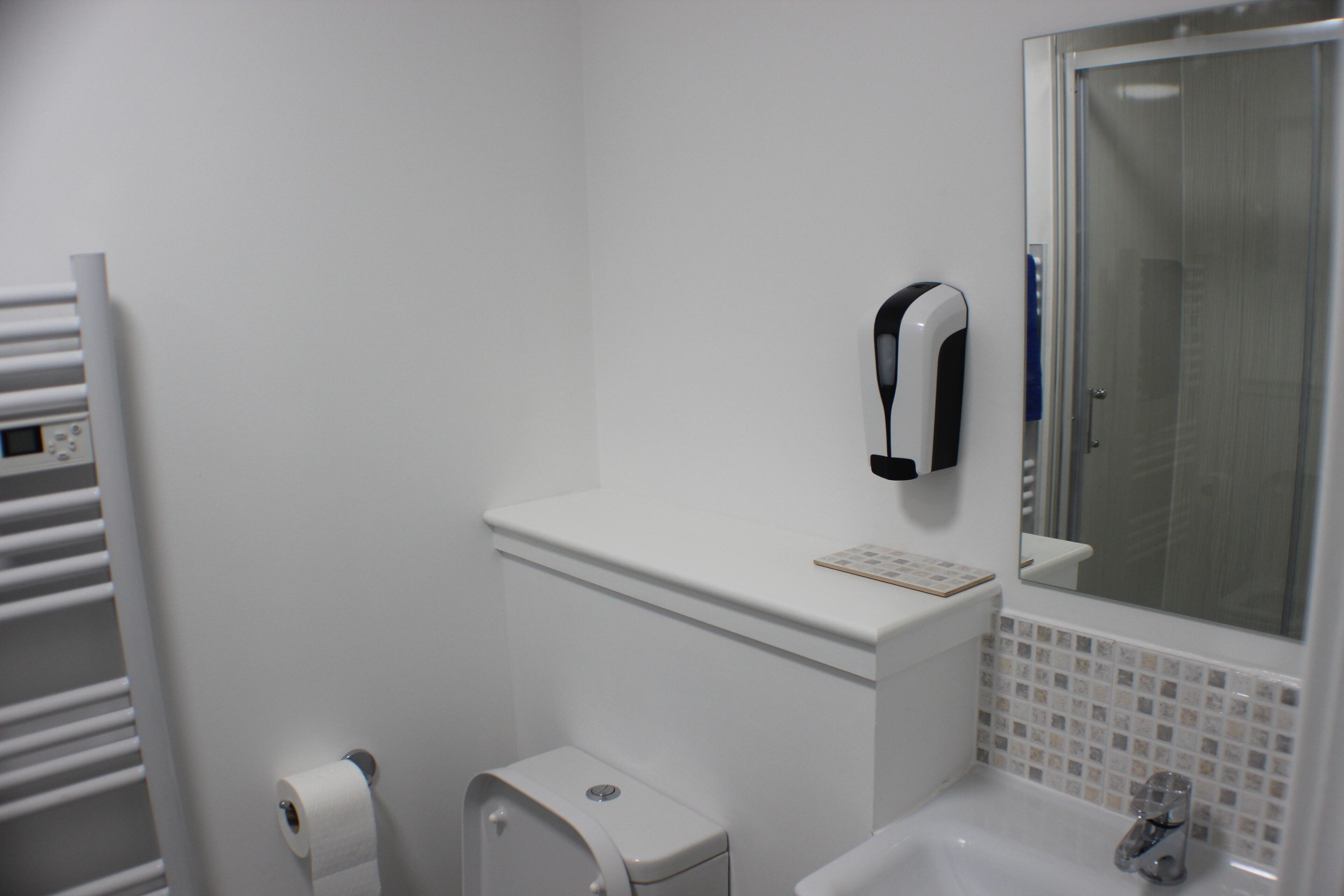 Un baño con inodoro, secamanos, lavabo y espejo.