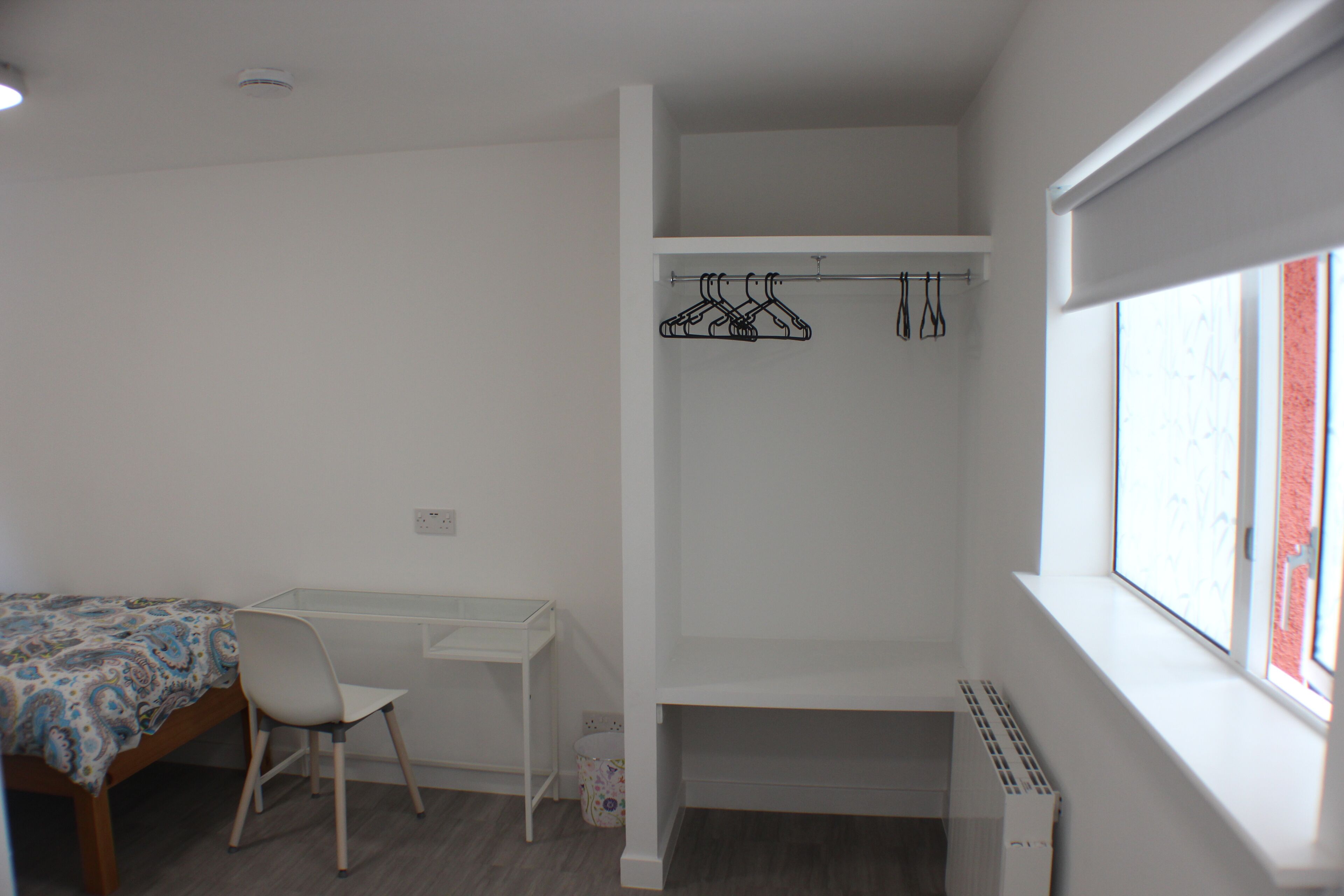A bedroom with a single bed, a desk, a chair, a radiator, and a window with a view.