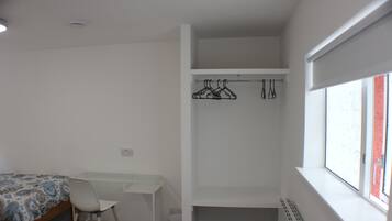 A bedroom with a single bed, a desk, a chair, a radiator, and a window with a view.