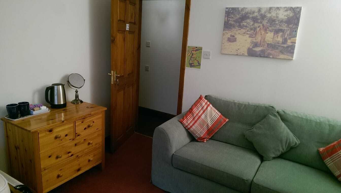 Une petite pièce agréable, avec une commode en bois, un canapé vert et une porte qui donne sur une autre pièce.