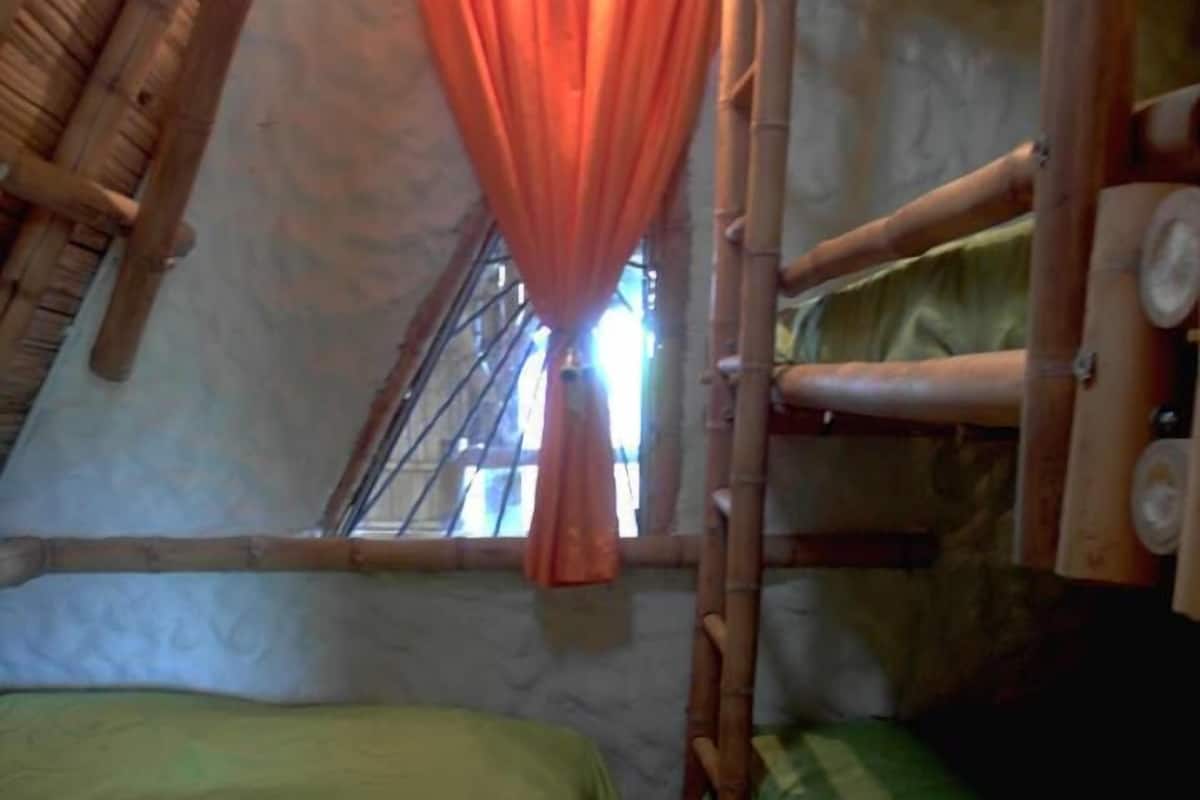 Ein Schlafsaalzimmer mit zwei Betten, einem Fenster mit Vorhang und einer Bambusleiter.