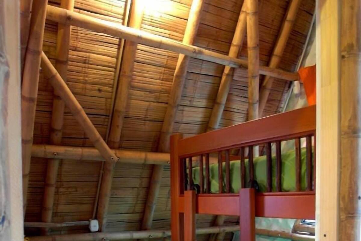 Ein kleiner, rustikaler Raum mit schrägem Dach und Holzbalken. Er enthält zwei Etagenbetten mit grüner Bettwäsche sowie einen kleinen Nachttisch mit einer Lampe.