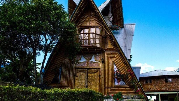 A wooden cabin with a steeply pitched roof, large windows, and a balcony. - Ecoturismo La Nohelia (Jericó)