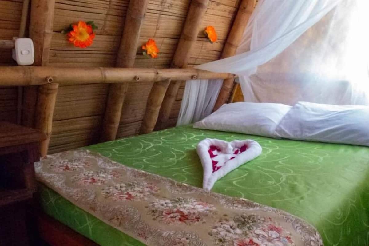 Ein Bett mit einer grünen Tagesdecke und einem herzförmigen Kopfkissen. Ein Holz-Kopfteil ist vorhanden und ein kleiner Tisch mit einem weißen Gegenstand darauf.