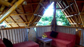 A room with a bamboo ceiling, red sofas, and a small wooden table with a decorative item. - Ecoturismo La Nohelia (Jericó)