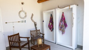 A room with a wooden bench, two chairs, a small table, and a refrigerator with colorful cloths.