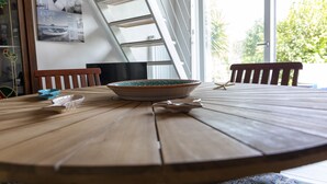 A wooden dining table with a bowl and a spoon, a chair, and a window with a view of greenery.