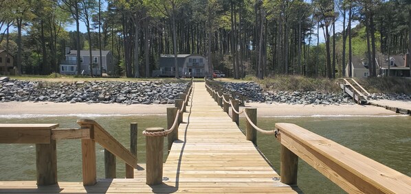 A wooden pier leading to a beach with houses in the background.