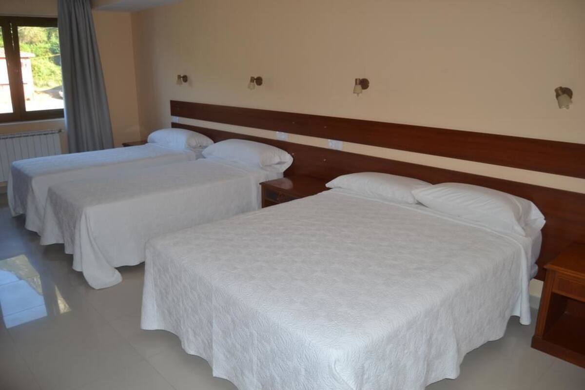 A hotel room with two single beds and a larger bed, all with white bedding.