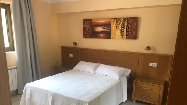 A bedroom with a large bed, wooden headboard, two bedside tables, and a wall-mounted painting.