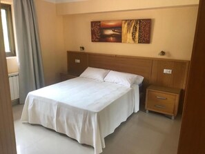 Un dormitorio con una cama grande, cabecera de madera, dos mesitas de noche y un cuadro colgado en la pared.