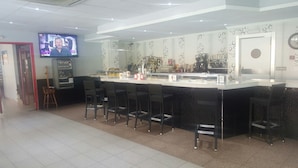 A modern bar area with a counter, bar stools, a television screen, and a jukebox.