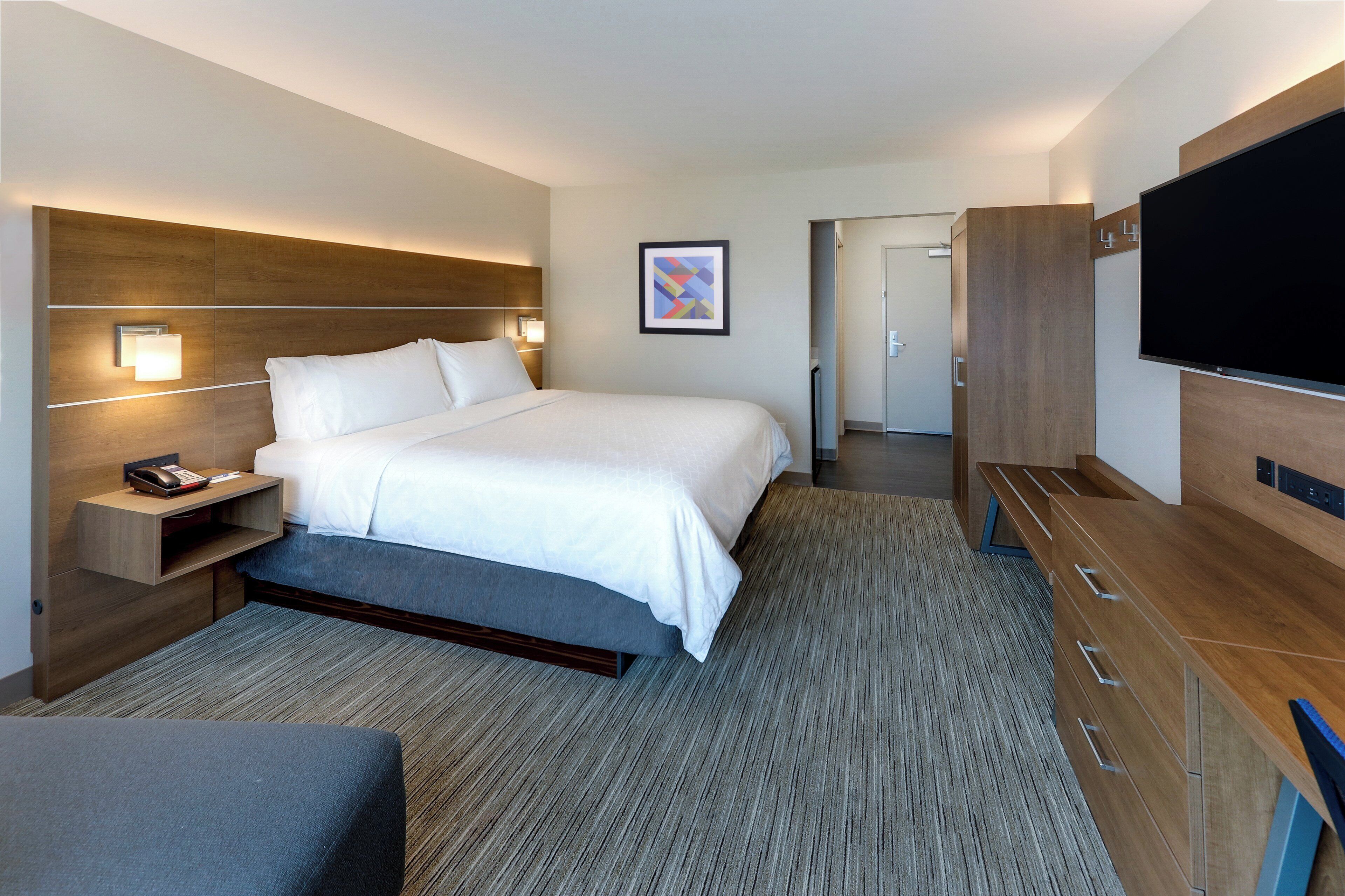 Une chambre d’hôtel moderne dotée d’un grand lit, de tables de chevet, d’un téléviseur à écran plat et d’une armoire en bois.