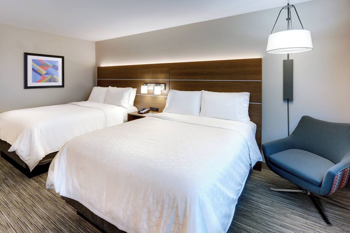 Una habitación de hotel con dos camas, un escritorio, una silla y una lámpara.