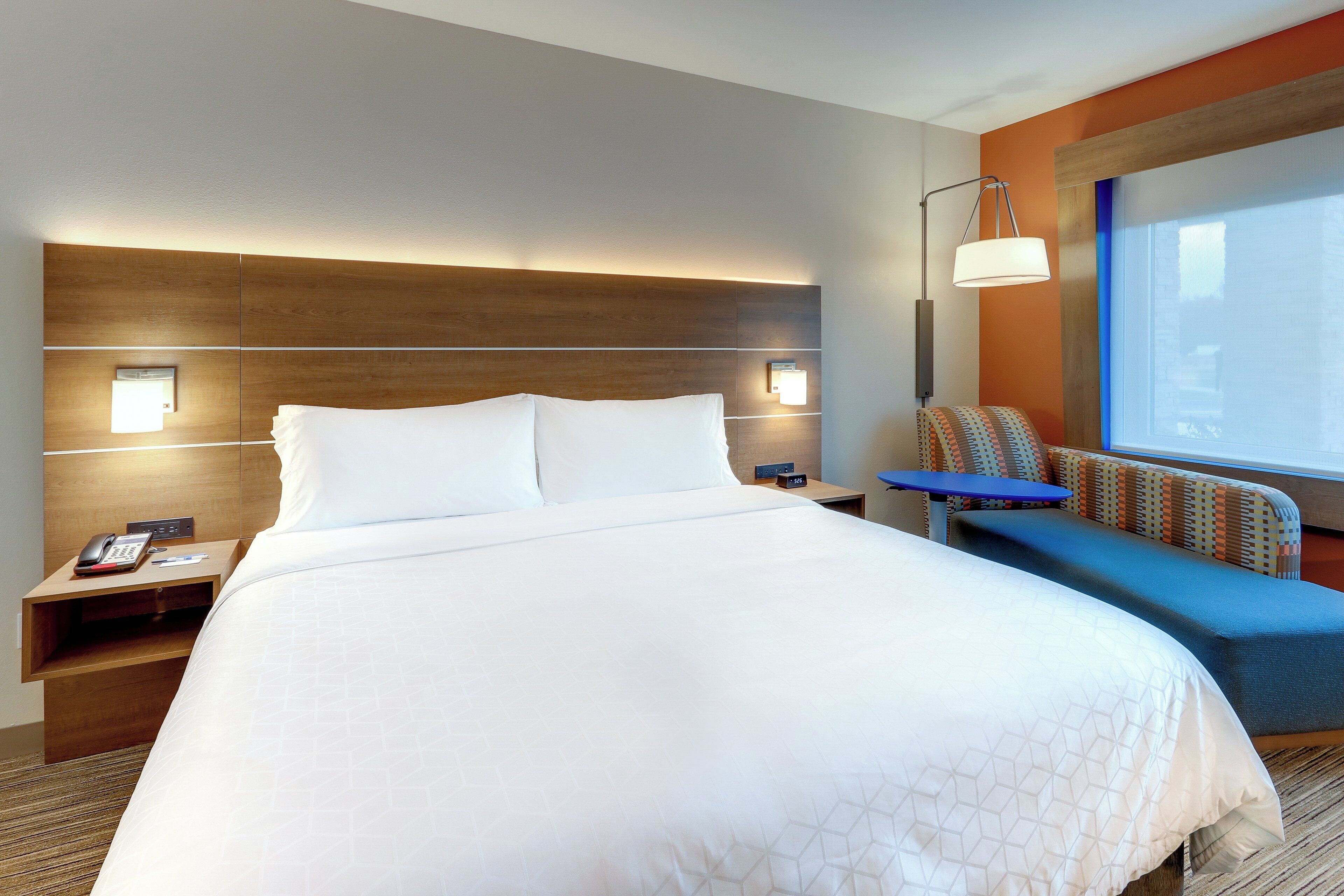 A hotel room with a large bed, a desk with a phone, a chair, and a window with a view.