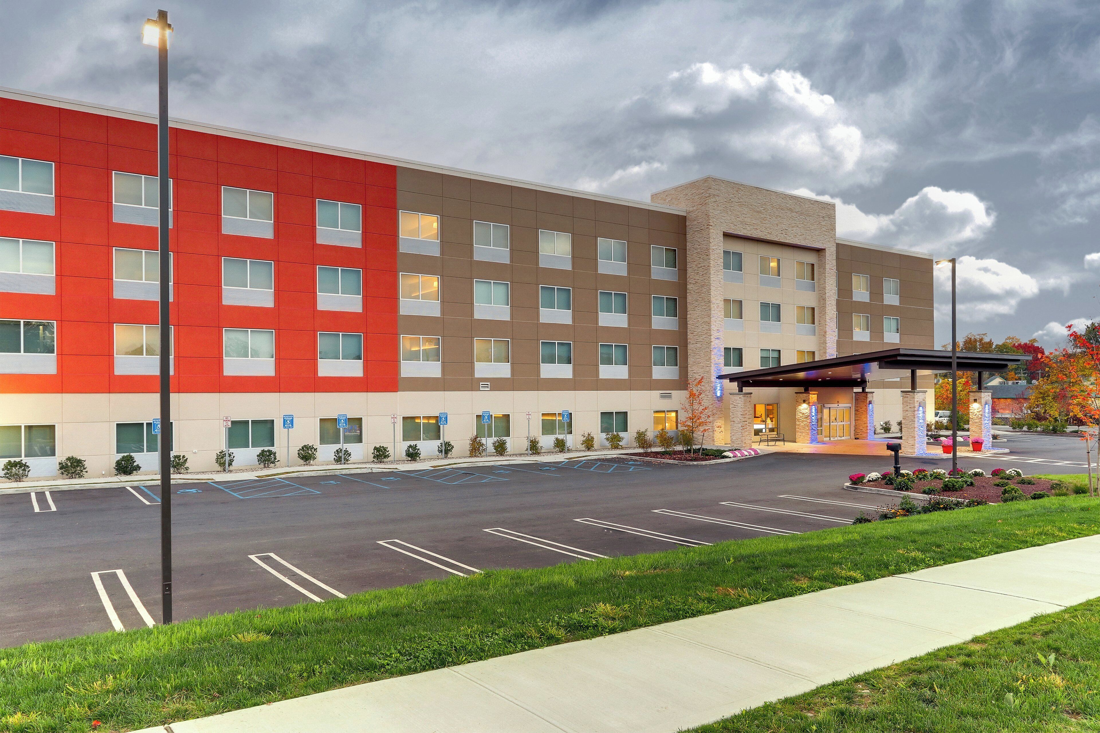A hotel with a red and beige facade, a parking lot, and a covered entrance area.