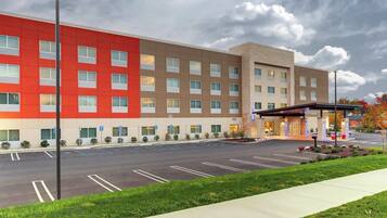 A hotel with a red and beige facade, a parking lot, and a covered entrance area.
