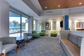 A hotel lobby with a seating area, large windows, and a patterned carpet.