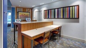 A modern reception area with a wooden desk, two chairs, a colorful striped artwork on the wall, and a patterned carpet. - Holiday Inn Express & Suites Middletown - Goshen by IHG (Middletown)