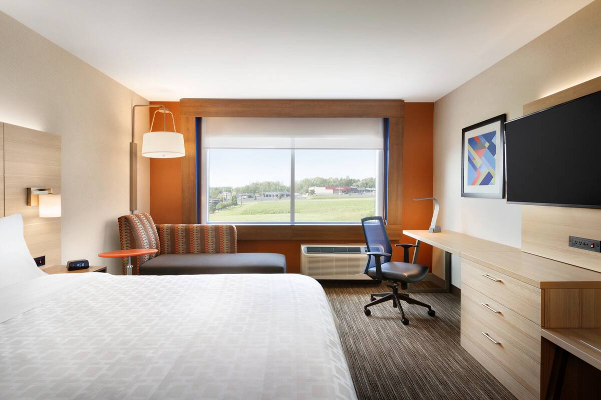 Habitación de hotel con una cama grande, un escritorio, una silla, un televisor y una ventana con vistas al exterior.