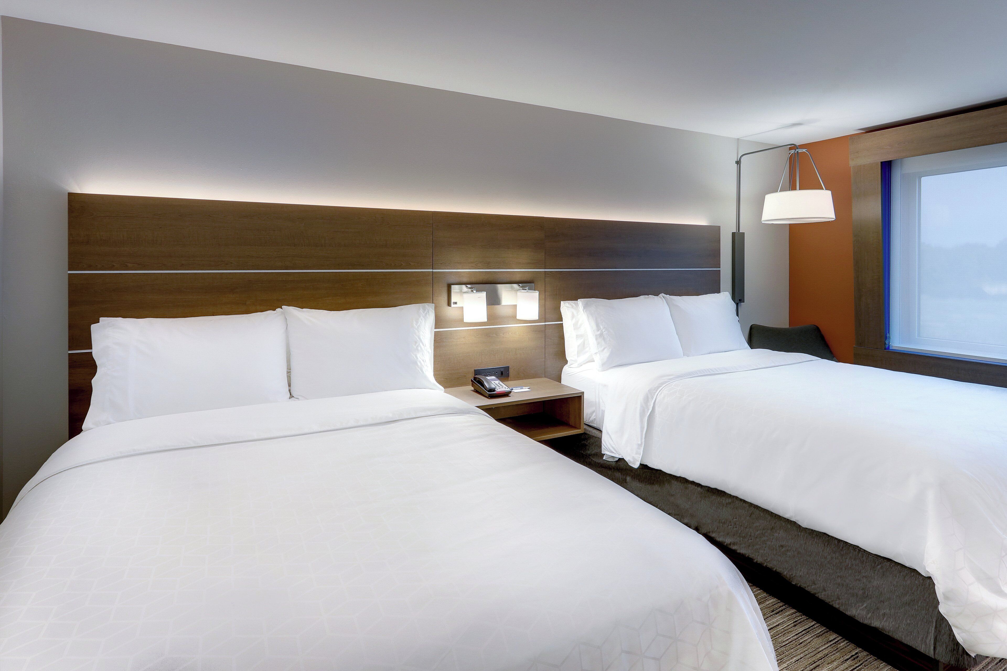 Une chambre d’hôtel avec deux lits, une table de chevet, une lampe et une fenêtre.