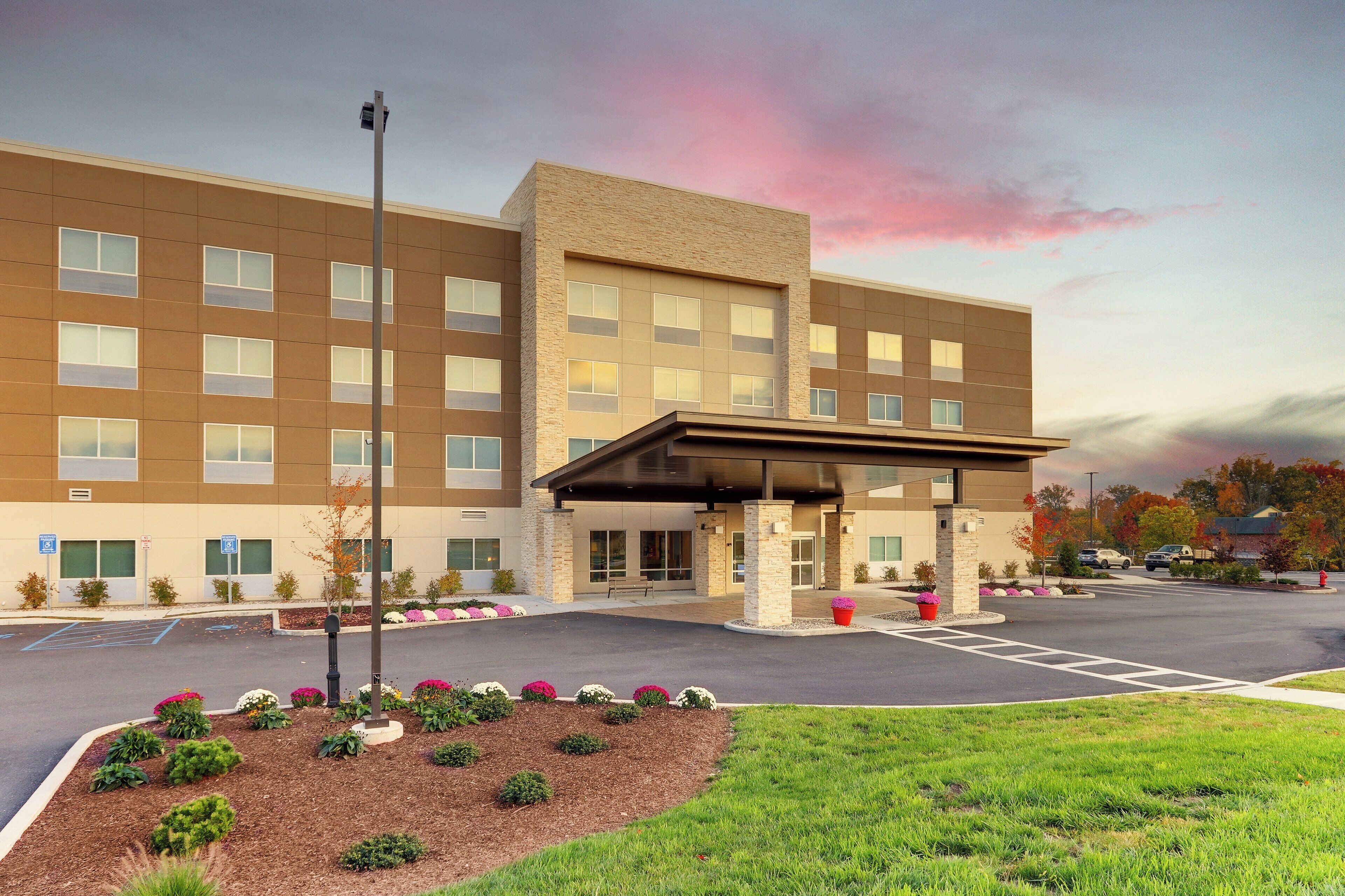 A modern hotel with a covered entrance, a parking lot, and landscaped areas with flowers.