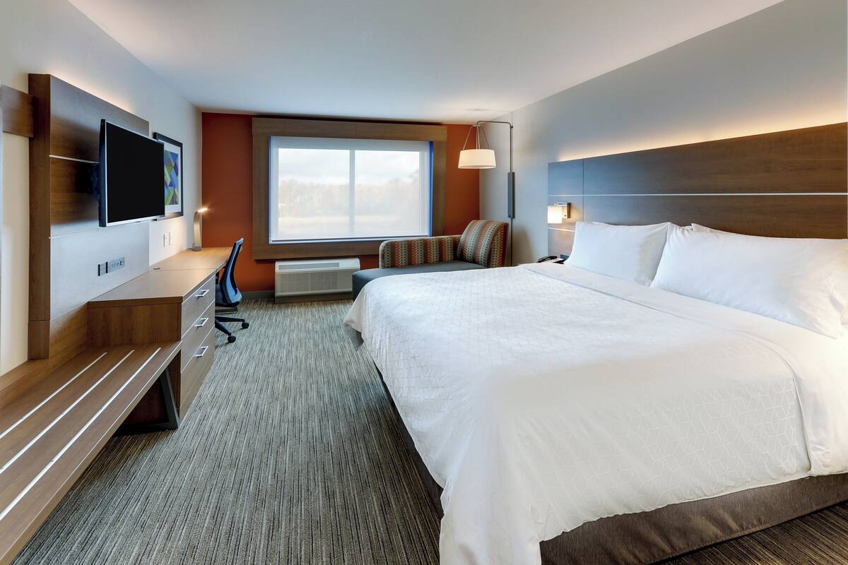Habitación de hotel con una cama grande, un escritorio con una silla, un televisor de pantalla plana montado en la pared y una ventana con vistas al exterior.
