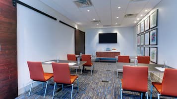 A conference room with a large flat-screen TV, multiple tables with chairs, and framed artwork on the walls.