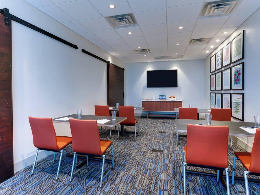 A conference room with a large flat-screen TV, multiple tables with chairs, and framed artwork on the walls.