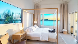 Un dormitorio moderno con una cama con dosel, una mesita de noche de madera, un escritorio y un amplio ventanal con vistas al mar.