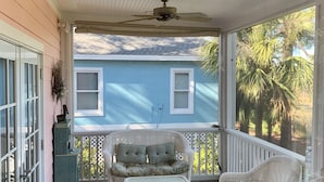 Un portico coperto con mobili in vimini, una ventola a soffitto e vista su una casa blu.