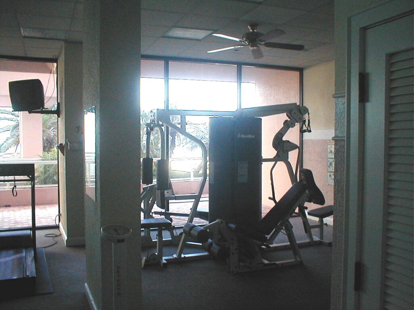 Ett gym med träningsutrustning, stora fönster och en takfläkt.