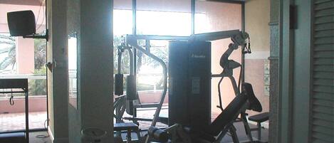 Ett gym med träningsutrustning, stora fönster och en takfläkt.