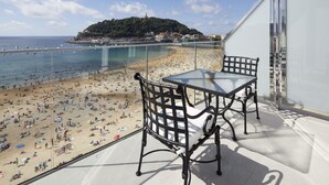 A balcony with a glass table and chairs overlooking a crowded beach with clear blue water and a hill in the background. - Hotel Villa Favorita - Adults Only (San Sebastián)