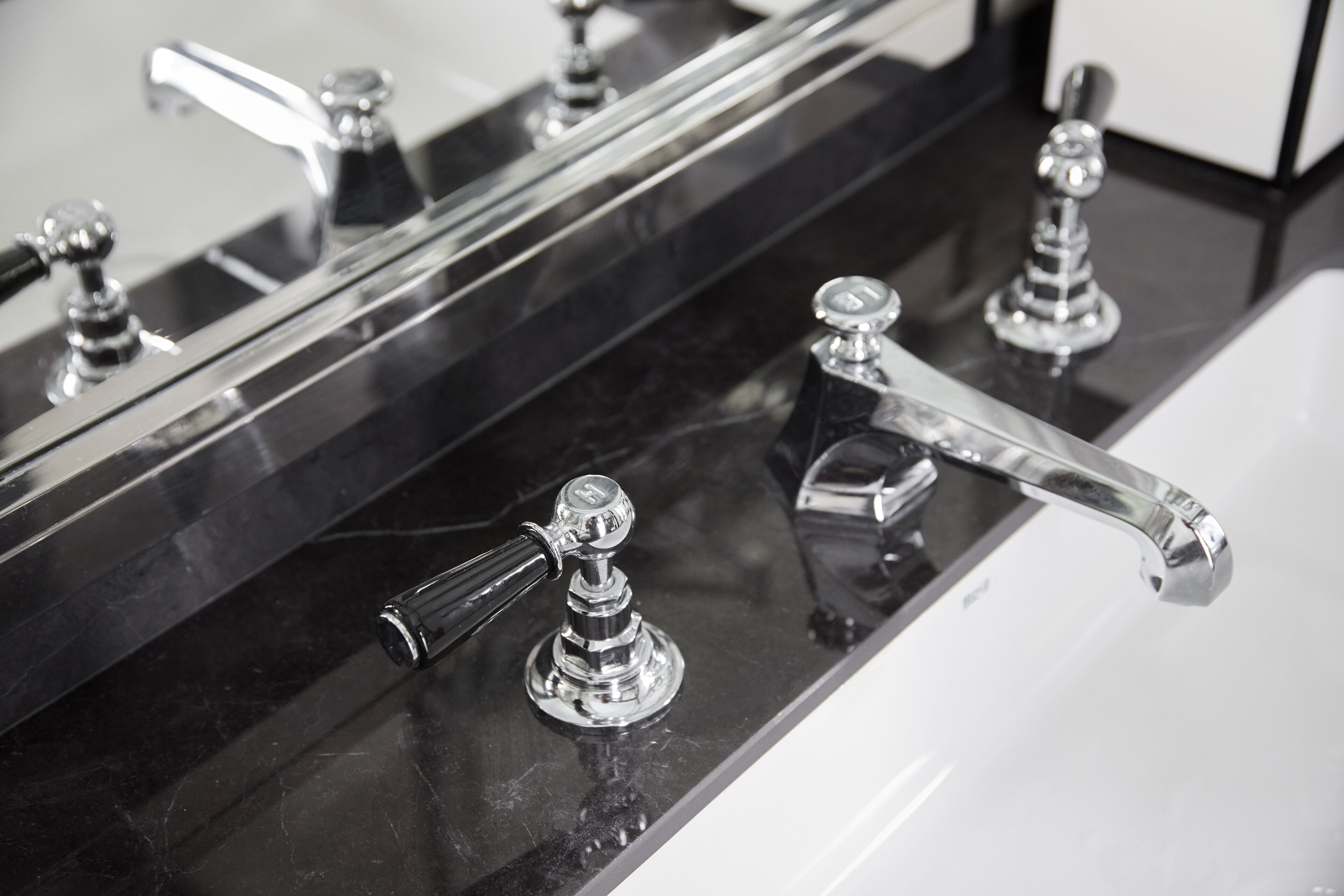 Un baño con encimera negra, lavabo blanco y grifos cromados.