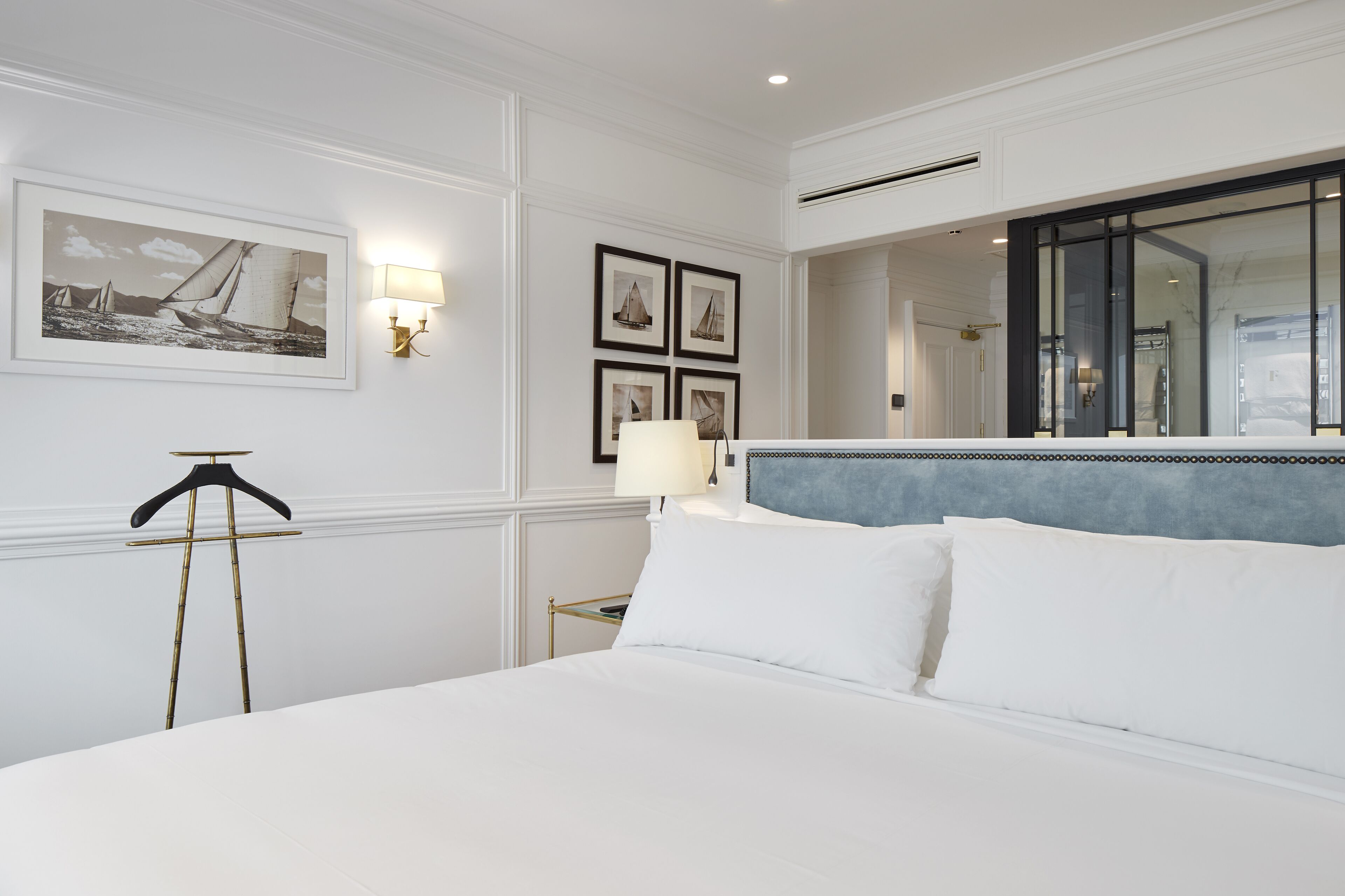Habitación de hotel con una cama grande, una mesita de noche, una lámpara, cuadros en la pared y un espejo.