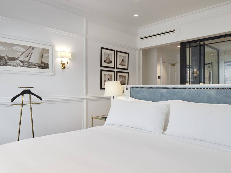 Habitación de hotel con una cama grande, una mesita de noche, una lámpara, cuadros en la pared y un espejo.