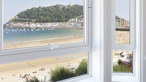 A room with large windows overlooking a beach, a wooden floor, and a small table. - Hotel Villa Favorita - Adults Only (San Sebastián)