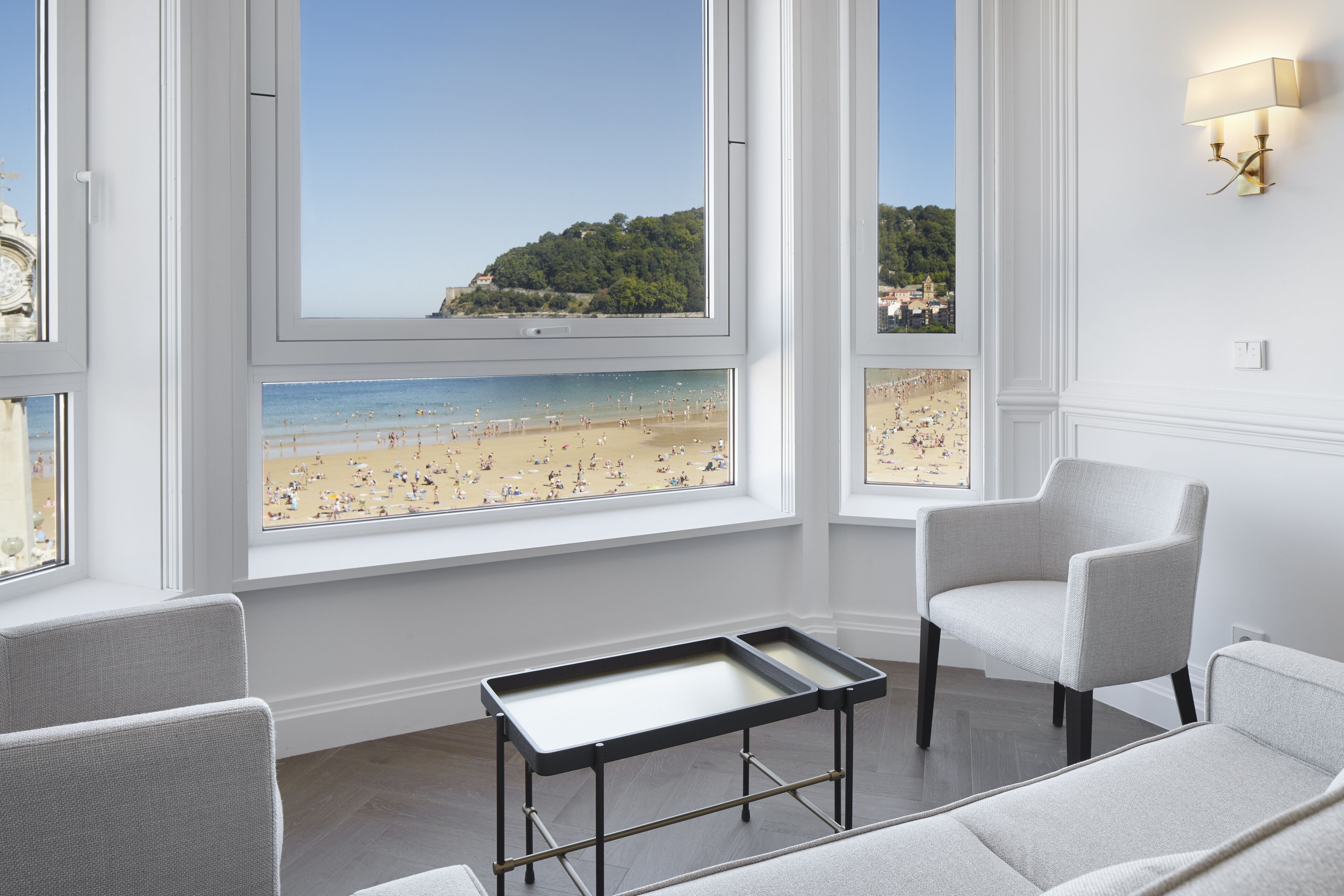 Una stanza con ampie finestre vista spiaggia, un tavolino e due sedie.