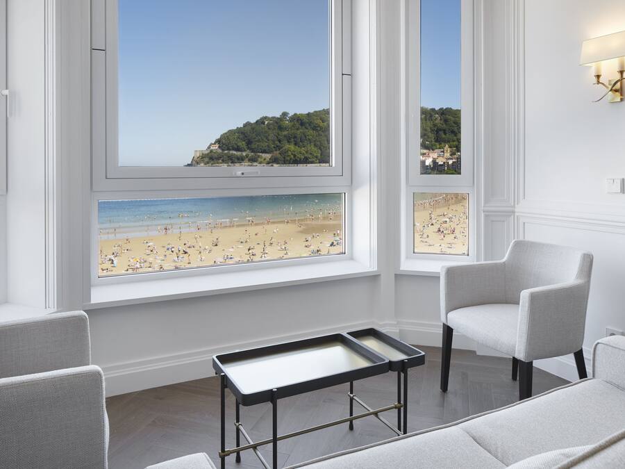 Una stanza con ampie finestre vista spiaggia, un tavolino e due sedie.