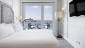 A hotel room with a large bed, a TV mounted on the wall, a balcony with a view of the sea, and a table with chairs. - Hotel Villa Favorita - Adults Only (San Sebastián)