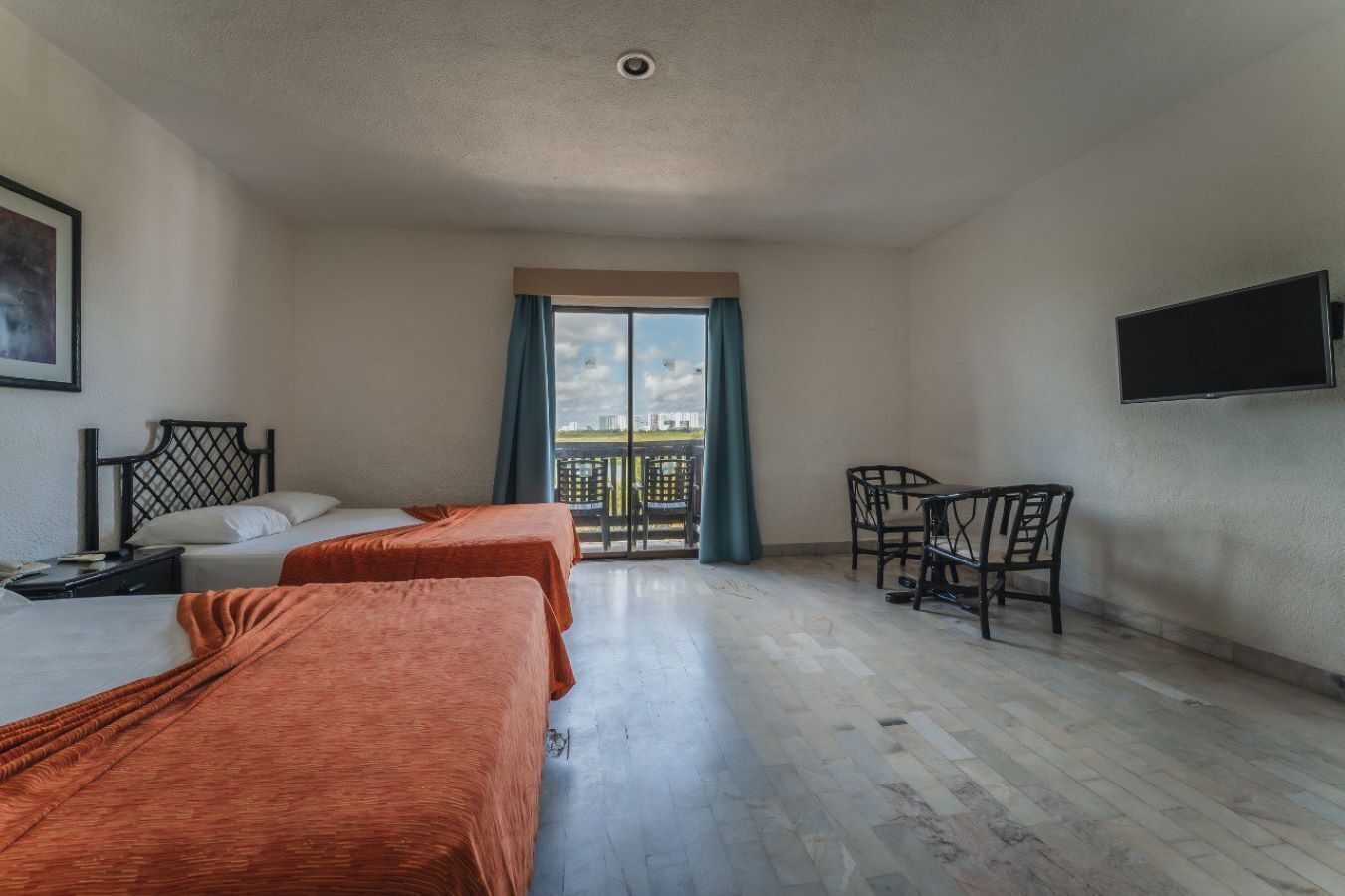A hotel room with two beds, a TV, a balcony with a view, and a chair.
