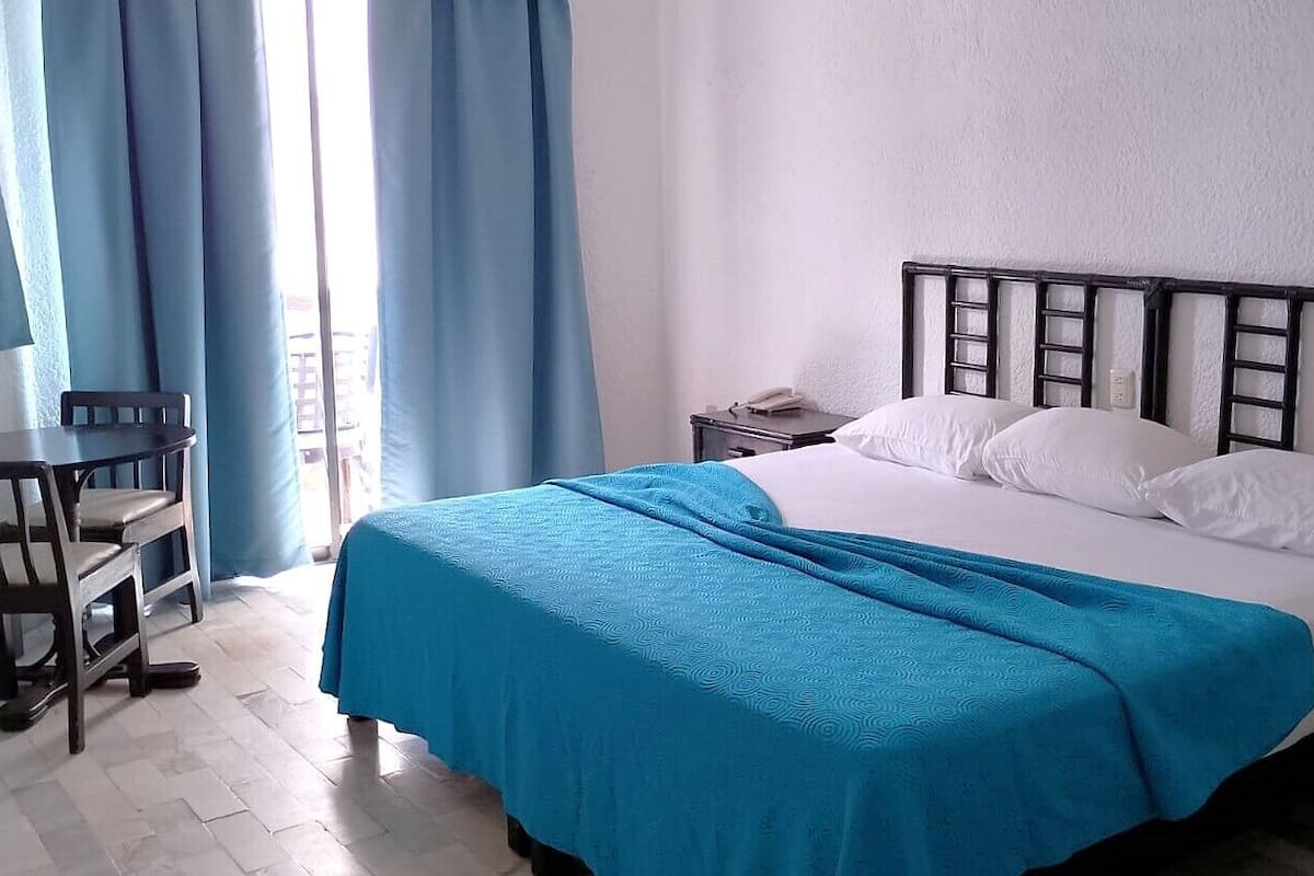 A bedroom with a bed, a nightstand, a chair, and a window with curtains.